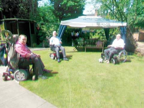 three residents in wheelchairs enjoying the garden sunshine and some sporting activity with a football